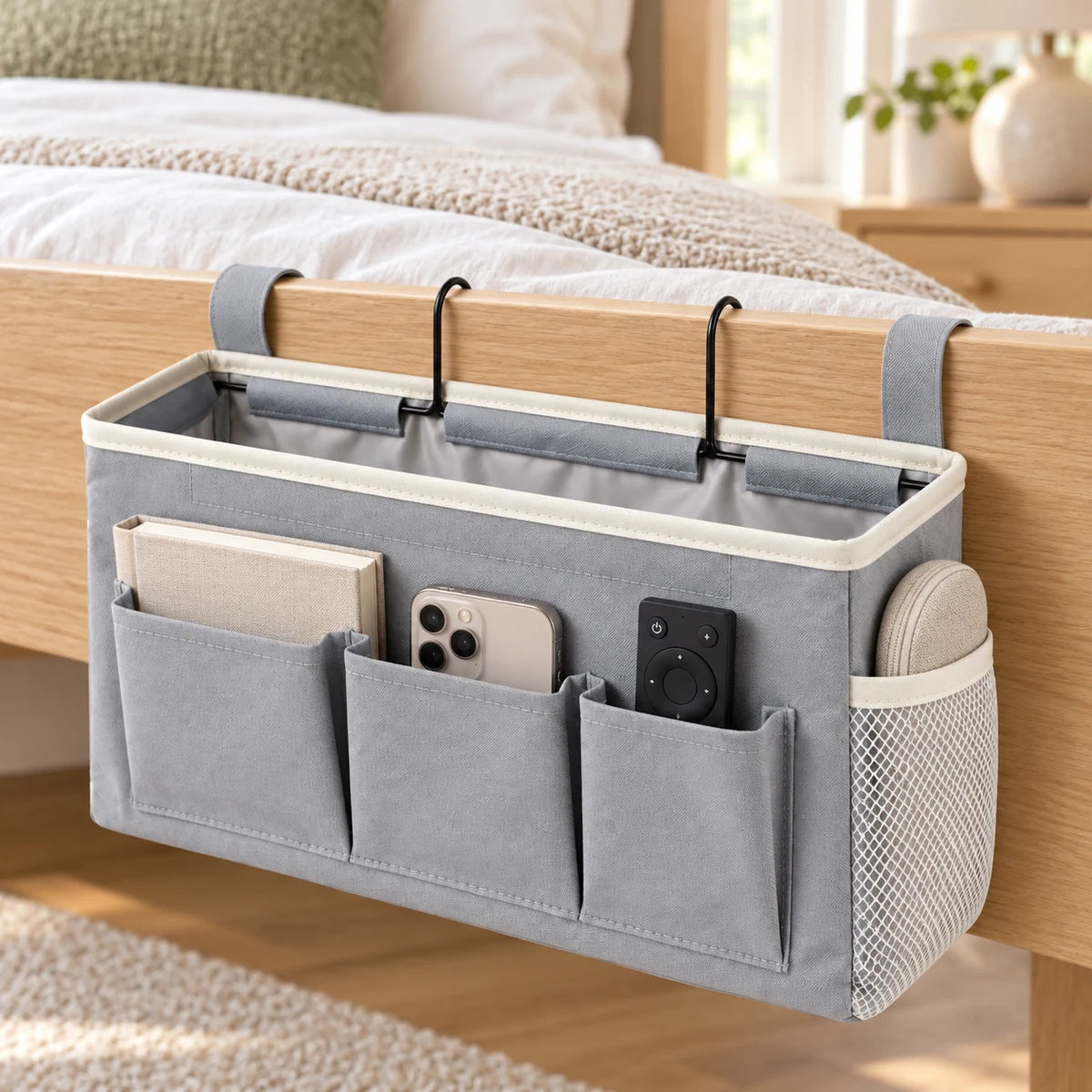 Gray bedside caddy organizer hanging from a light wood bed frame with daily essentials